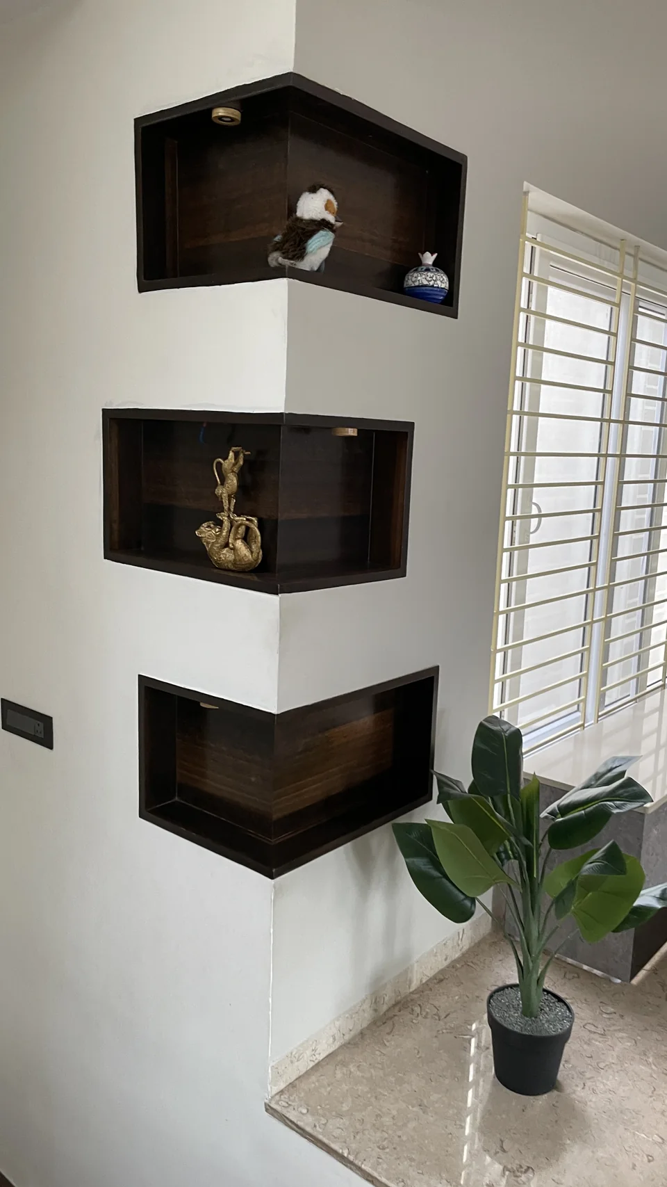 Three dark timber niches set into a white corner beside a window