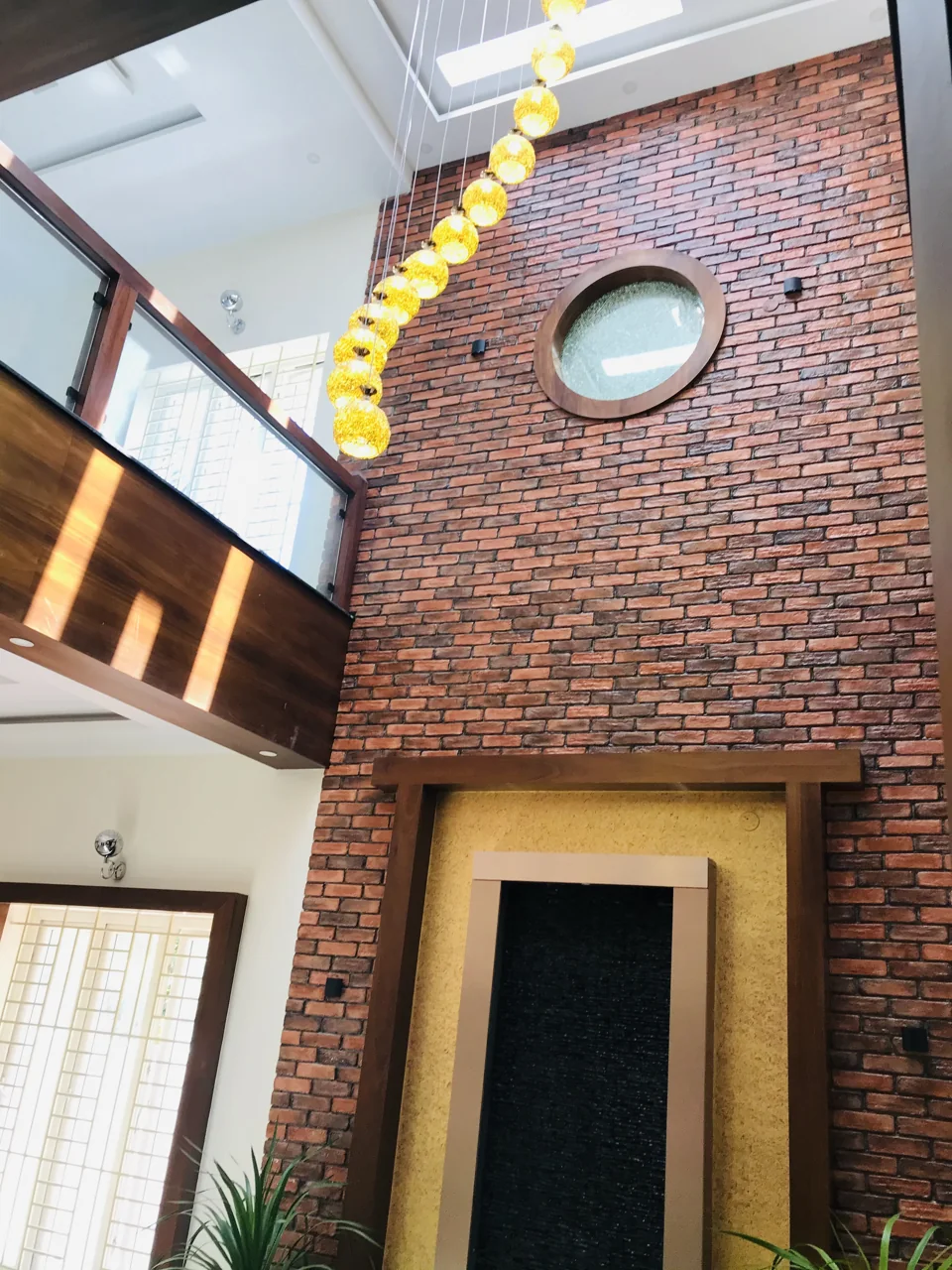Brick feature wall with a round window, a cascading pendant and a framed doorway