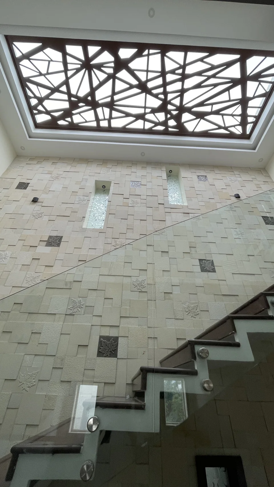 Stone-clad stair wall with a glass balustrade under a patterned ceiling cut-out